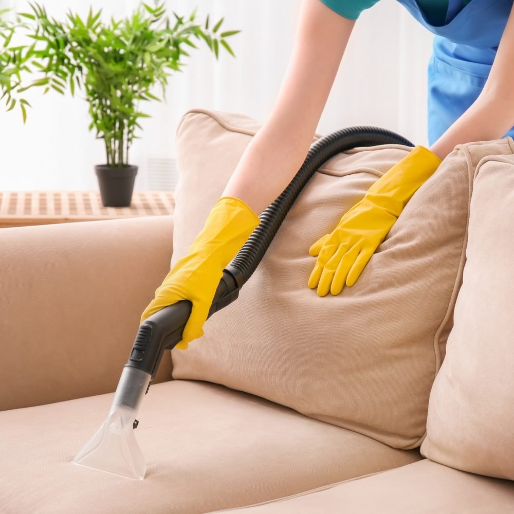 Woman cleaning couch with vacuum cleaner at home